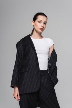 Beyaz tişörtlü ve takım elbiseli moda kadın gri üzerinde yalnız poz veriyor. 