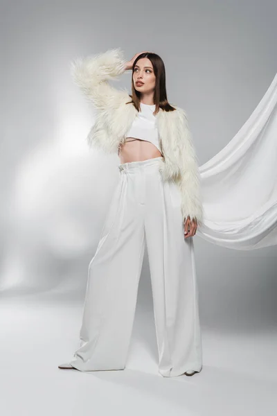 Модная Женщина Искусственном Меховом Пиджаке Белых Брюках Позирует Абстрактном Сером — стоковое фото
