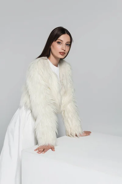 Young Woman Faux Fur Jacket Looking Camera Leaning White Cube — Stock Photo, Image