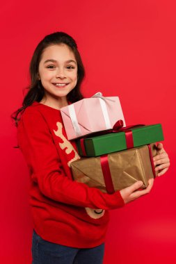 Kış süveteri içinde neşeli bir kız elinde bir sürü Noel hediyesi ve kıpkırmızı bir gülümseme tutuyor.