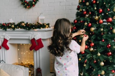 Pijamalı çocuk oturma odasında Noel ağacı süslüyor. 