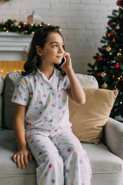 Evde Noel kutlaması sırasında pijamalı bir çocuk akıllı telefonuyla koltukta konuşuyor. 