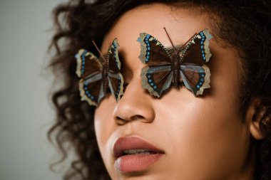 Gri renkli gözlerinde kelebekler olan kıvırcık Afrikalı Amerikalı kadına yakın durun.