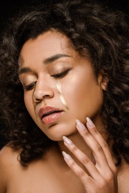 Yanaklarında altın gözyaşları olan siyah yüzlere dokunan Afrikalı Amerikalı kadın. 