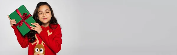 Uśmiechnięta Dziewczyna Swetrze Trzyma Świąteczny Prezent Izolowany Szarości Sztandar — Zdjęcie stockowe