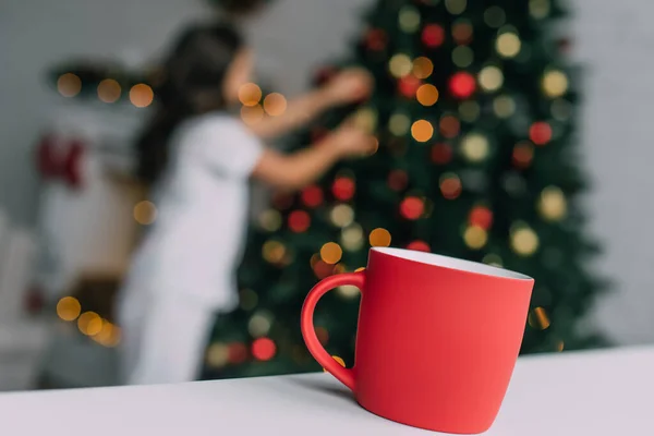 Piros Csésze Asztalon Közelében Elmosódott Lány Karácsonyfa Otthon — Stock Fotó