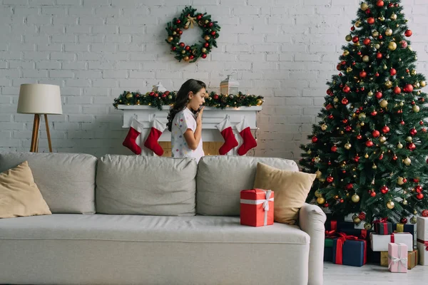 Side view of shocked preteen child looking at presents under Christmas tree at home