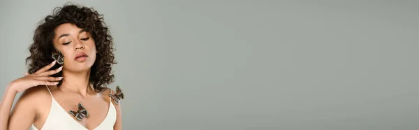 Кучерява Афроамериканська Жінка Метеликами Тілі Щокою Позує Ізольовано Сірому Банер — стокове фото