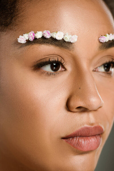 close up view of pretty african american woman with flowers on eyebrows