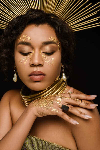 young african american woman with golden crown and paint on face posing isolated on black