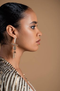 side view of young african american woman in luxurious golden jewelry isolated on beige  clipart