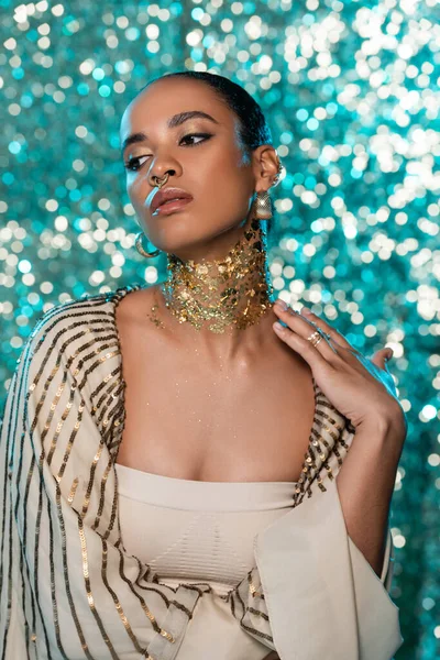 sensual african american woman with shiny shawl and gold on neck posing on sparkling blue background