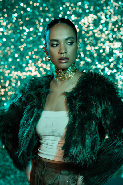 young african american woman in faux fur jacket and gold on neck posing on sparkling blue background 