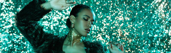 стильная африканская американка в искусственной меховой куртке и золотом на шее позирует на блестящем голубом фоне, баннер 