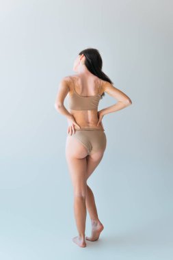 Vitiligo 'lu genç bir kadının arkası. Elleri gri kalçaların üzerinde duruyor.