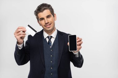 Telli neşeli iş adamı elinde boş ekranlı akıllı telefon ve gri ekranlı kredi kartı tutuyor. 