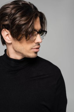 brunette man in black turtleneck and eyeglasses posing isolated on grey clipart