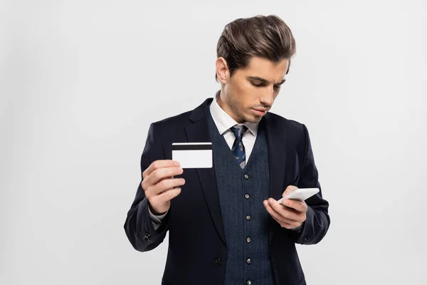 スマートフォンでスーツ姿のビジネスマンがグレーで隔離されたクレジットカードを持ち — ストック写真