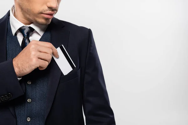 スーツ姿の若いビジネスマンがクレジットカードをポケットに入れグレーで隔離された — ストック写真