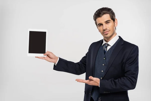 スーツ姿の若いビジネスマンがグレーで隔絶された空白の画面でデジタルタブレットを指して — ストック写真