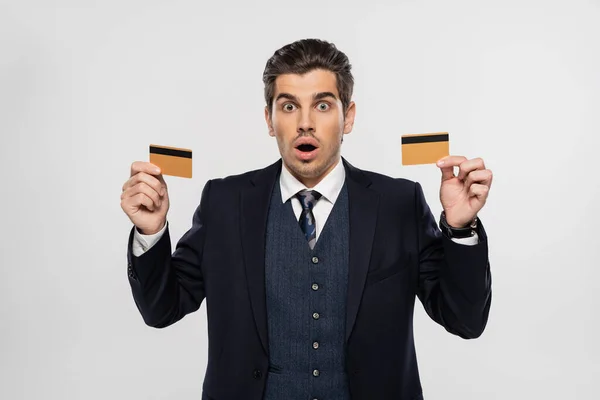 Zszokowany Biznesmen Garniturze Trzymający Karty Kredytowe Odizolowane Szaro — Zdjęcie stockowe