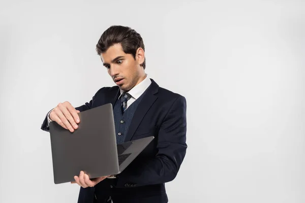 スーツ姿のビジネスマンがグレーで隔離されたノートパソコンを見てショックを受け — ストック写真