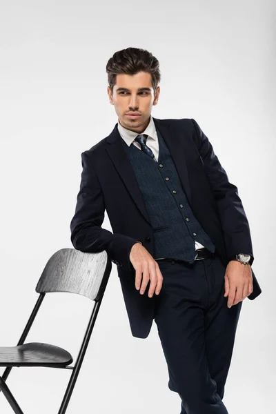 穿着正式服装的年轻商人站在椅子旁边 孤零零地看着灰色的椅子 — 图库照片