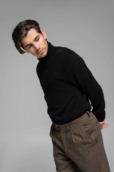 good looking man in black turtleneck looking away while posing isolated on grey