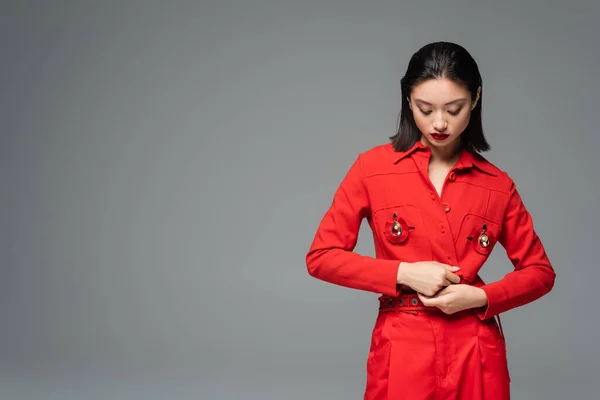 stock image brunette asian woman touching red jacket decorated with brooches isolated on grey