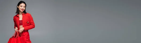 Улыбающаяся Азиатка Стильной Куртке Красными Сумками Покупок Смотрящая Камеру Изолированную — стоковое фото