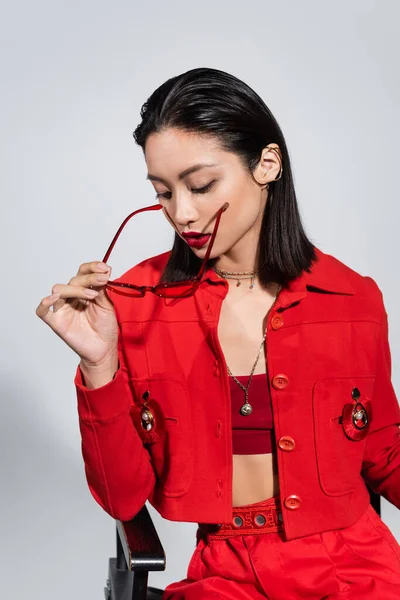 Morena Asiático Mulher Vermelho Jaqueta Segurando Moda Óculos Sol Isolado — Fotografia de Stock