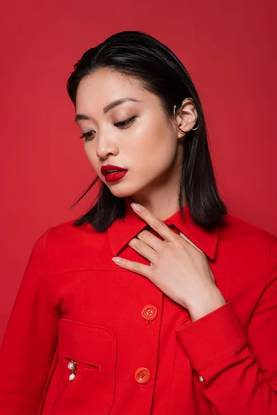 性感的亚洲女人 穿着时髦的夹克和耳朵袖口 手放在胸前 与红色隔离 — 图库照片