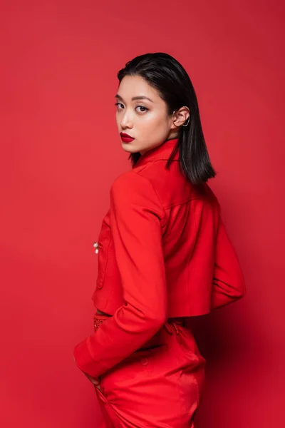Aasialainen Nainen Tyylikkäissä Vaatteissa Seisoo Käsi Taskussa Katselee Kameraa Punaisella — kuvapankkivalokuva