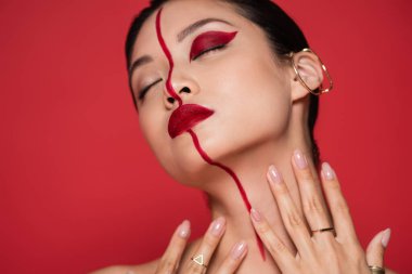 Baştan çıkarıcı kulaklıklı, yaratıcı makyajlı, gözleri kapalı ve elleri boyuna yakın kırmızı elbiseli Asyalı kadın.