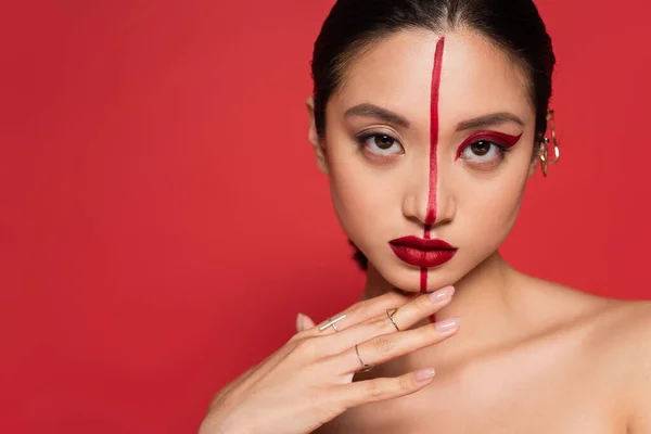 stock image portrait of asian woman with creative visage touching chin and looking at camera isolated on red