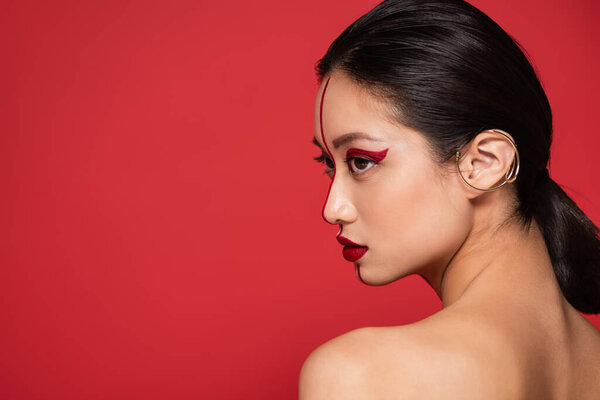 profile of sensual asian woman with creative makeup looking away isolated on red