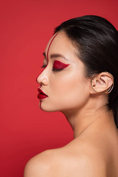 profile of asian woman with closed eyes and artistic makeup on perfect face isolated on red