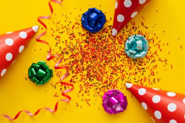 Top view of dotted party caps near gift bows and sprinkles on yellow background  clipart