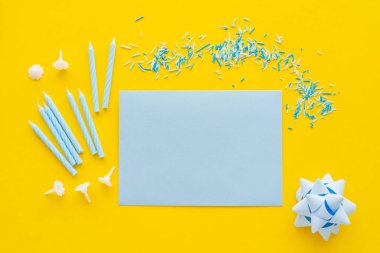 Top view of empty greeting card near candles and blue sprinkles on yellow background  clipart