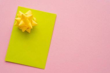 Sarı boş tebrik kartının üst görüntüsü ve pembe arka planda hediye yayı 