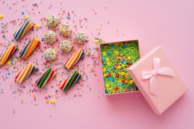 Pembe arka planda serpiştirilmiş hediye kutusunun yanındaki renkli şekerlerin üst görünümü 