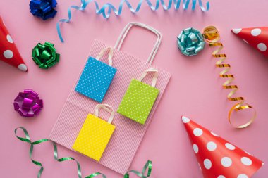Parti şapkaları ve pembe arka planda yılan balığının yanındaki alışveriş çantalarının en üst görüntüsü 