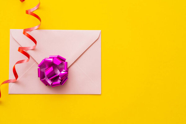 Вид сверху на эмблему и подарочный лук возле серпантина на желтом фоне 