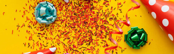 Вид сверху на партийные фуражки возле посыпанных и подарочных ботинок на желтом фоне, баннер 
