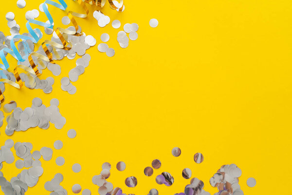 Вид сверху на разноцветные серпантин и конфетти на желтом фоне 