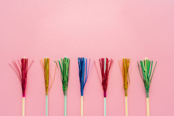 Top view of drinking straws with colorful tinsel on pink background with copy space