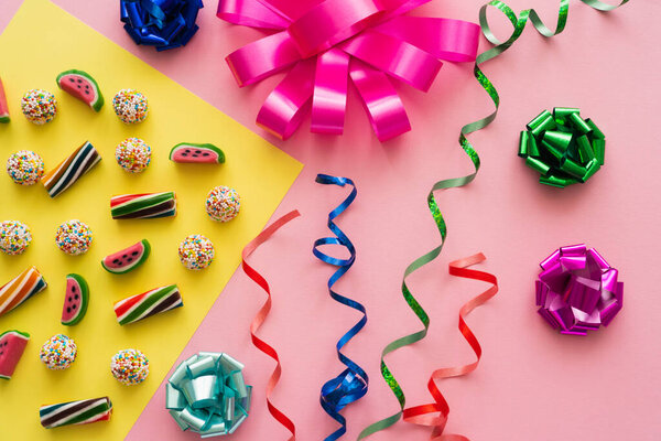 Вид сверху на конфеты возле серпантина и подарочные киоски на розовом фоне 