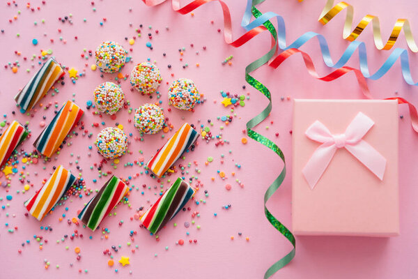 Вид сверху подарочной коробки возле серпантина и цветные конфеты на розовом фоне 