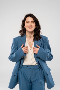 Boncuklu ve mavi takım elbiseli mutlu esmer kadın. Gri gözleri kapalı duruyor.