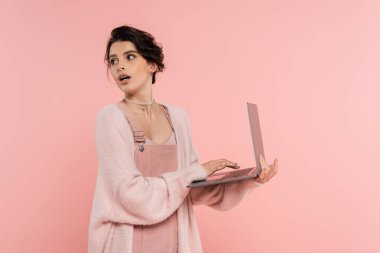 Dizüstü bilgisayarı olan esmer kadın arkasına bakıyor. Pembe üzerine izole edilmiş.
